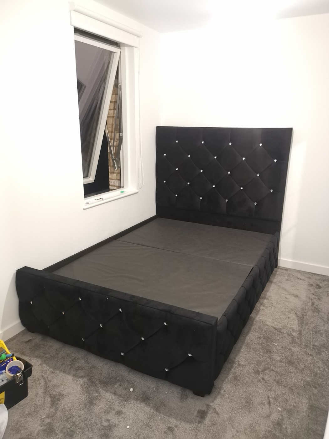 A black crushed-velvet upholstered double bed with a buttoned headboard, fully assembled in a bedroom by Swift Handy Works.