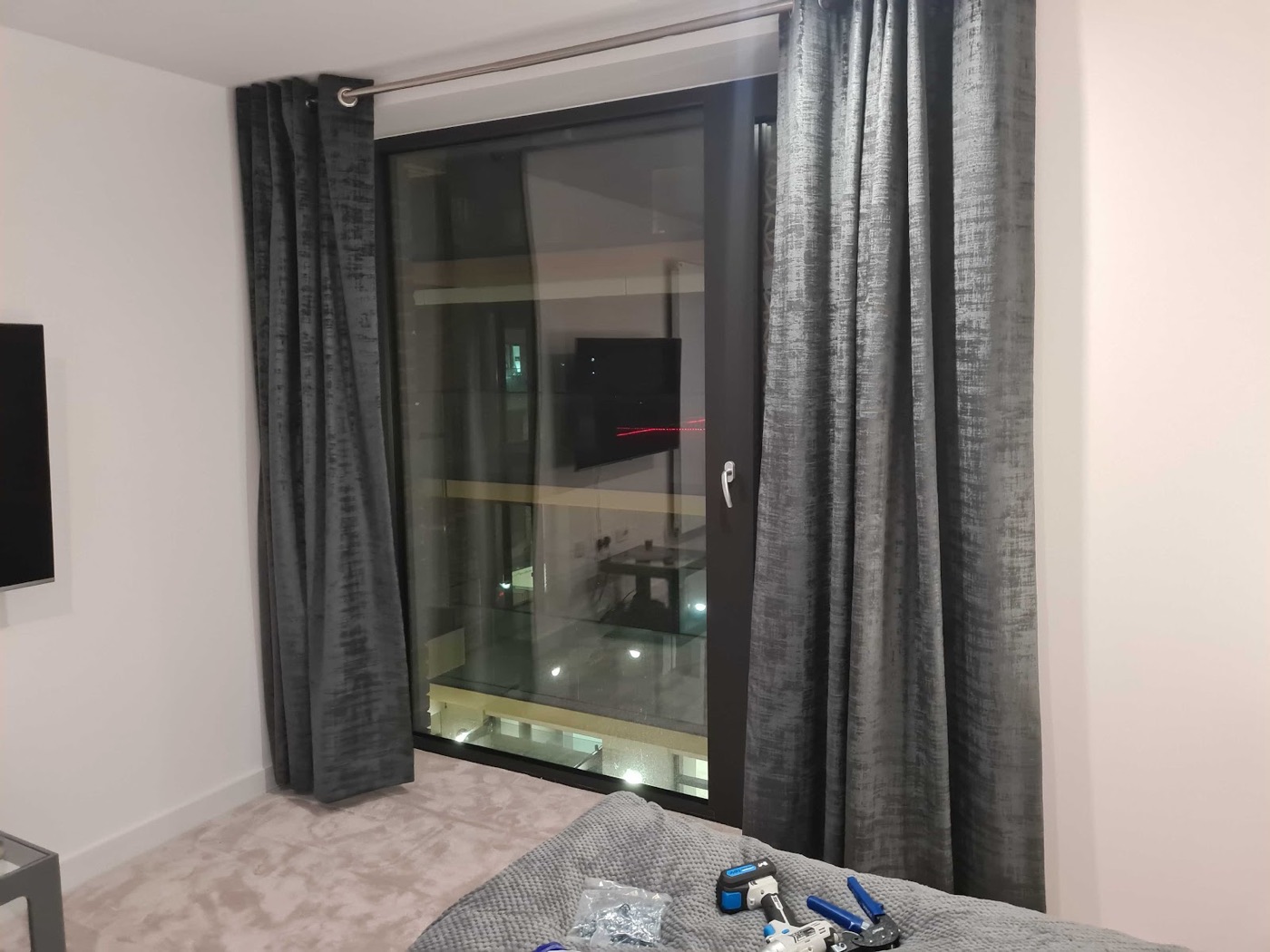 Full-height grey velvet curtains hung on a newly fitted pole across a floor-to-ceiling apartment window by Swift Handy Works.