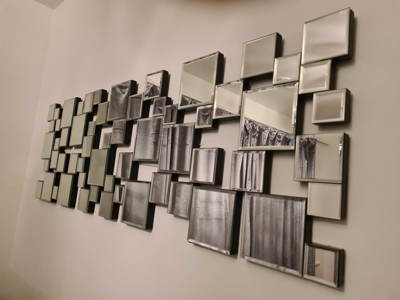 A large multi-panel bevelled mirror feature wall installed by Swift Handy Works, dozens of square mirrors hung perfectly aligned on a living-room wall.