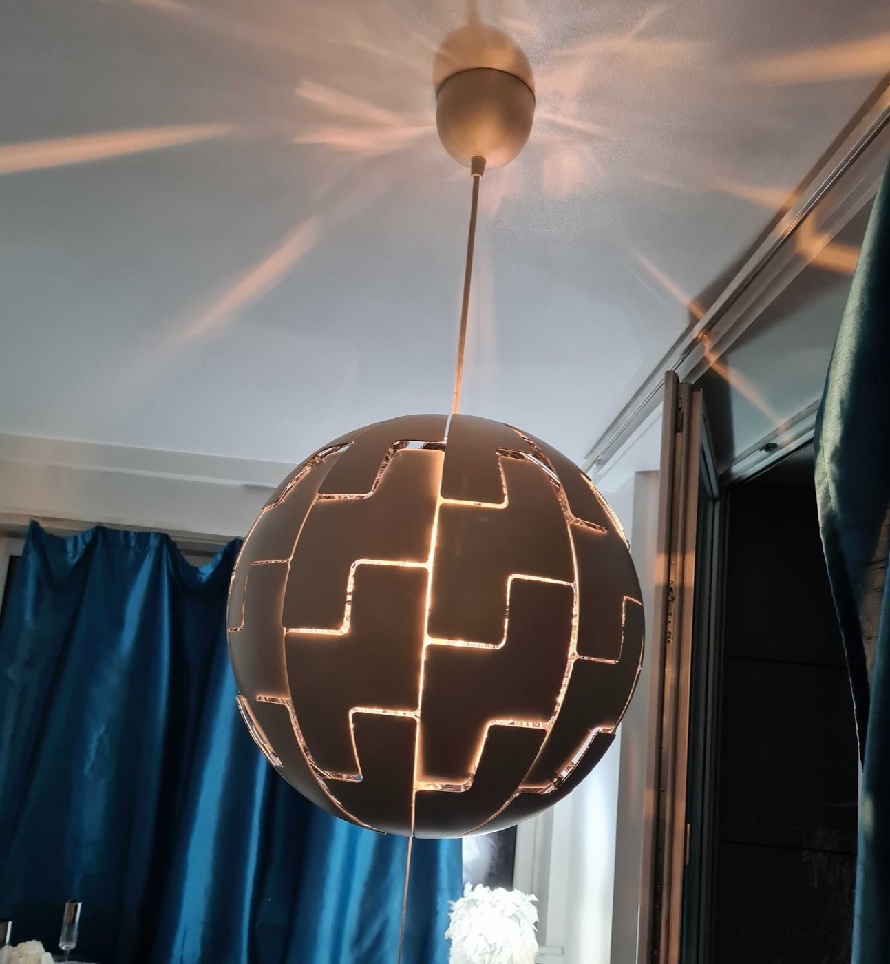 A spherical pendant light fitting installed on a ceiling by Swift Handy Works, switched on and casting a warm patterned glow.