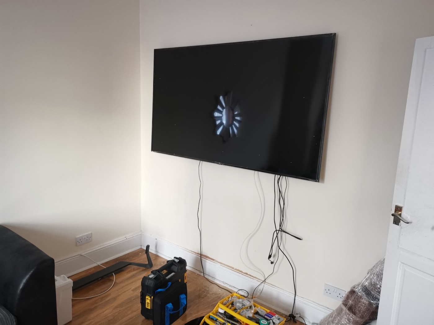 A large flat-screen TV freshly mounted on a living-room wall by Swift Handy Works, with the tool case open below and cables still to be tidied.